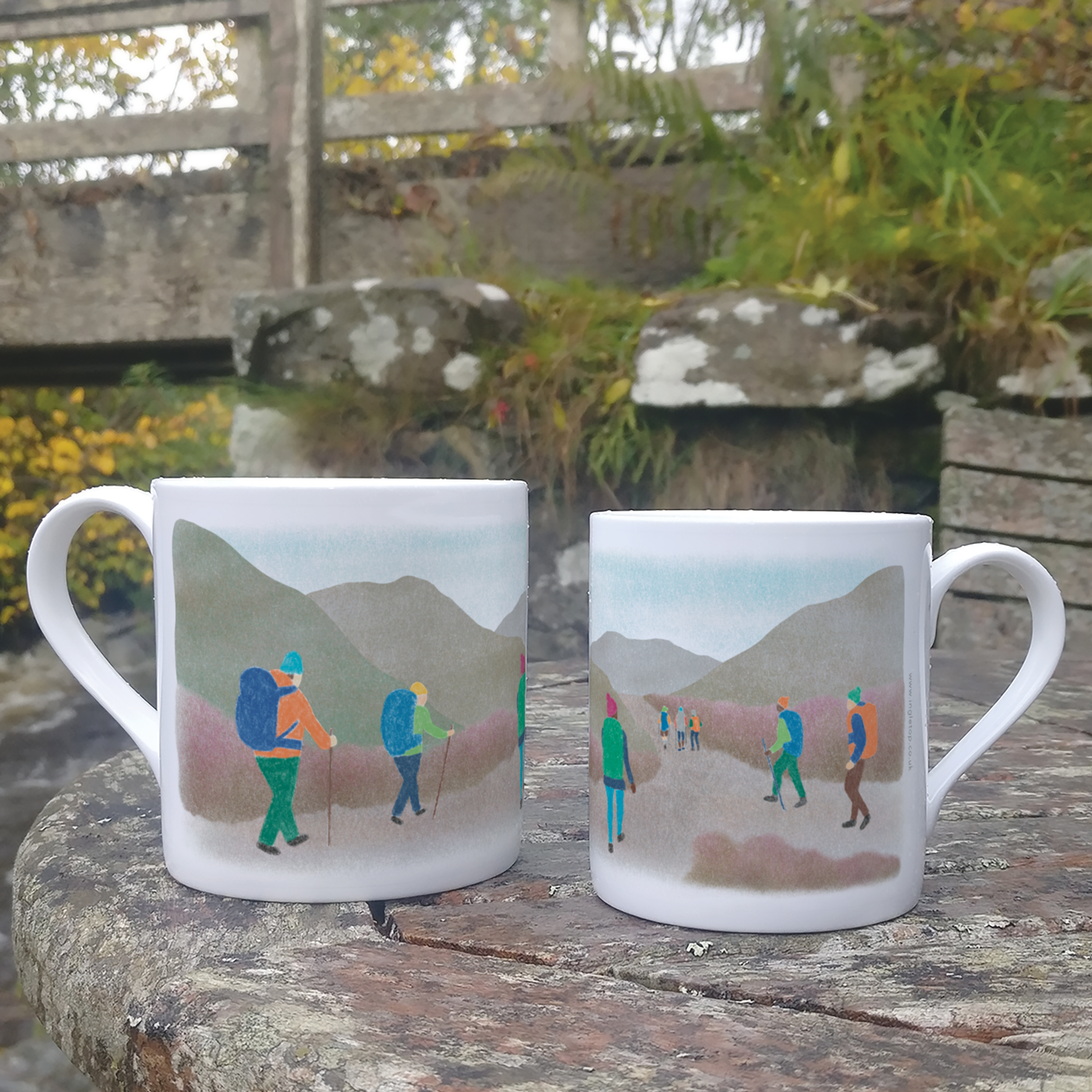 A size comparison of two china mugs, each decorated with an illustration of eight hikers, displayed on an outdoor table