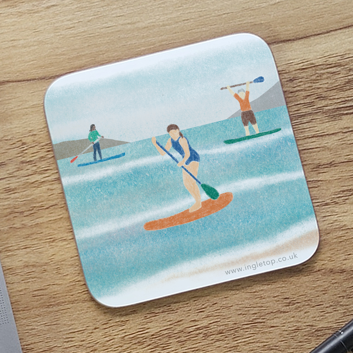 A paddleboarding coaster on a wooden desk top 