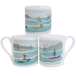 A stack of three white china mugs, decorated with a colourful illustration of people using paddleboards