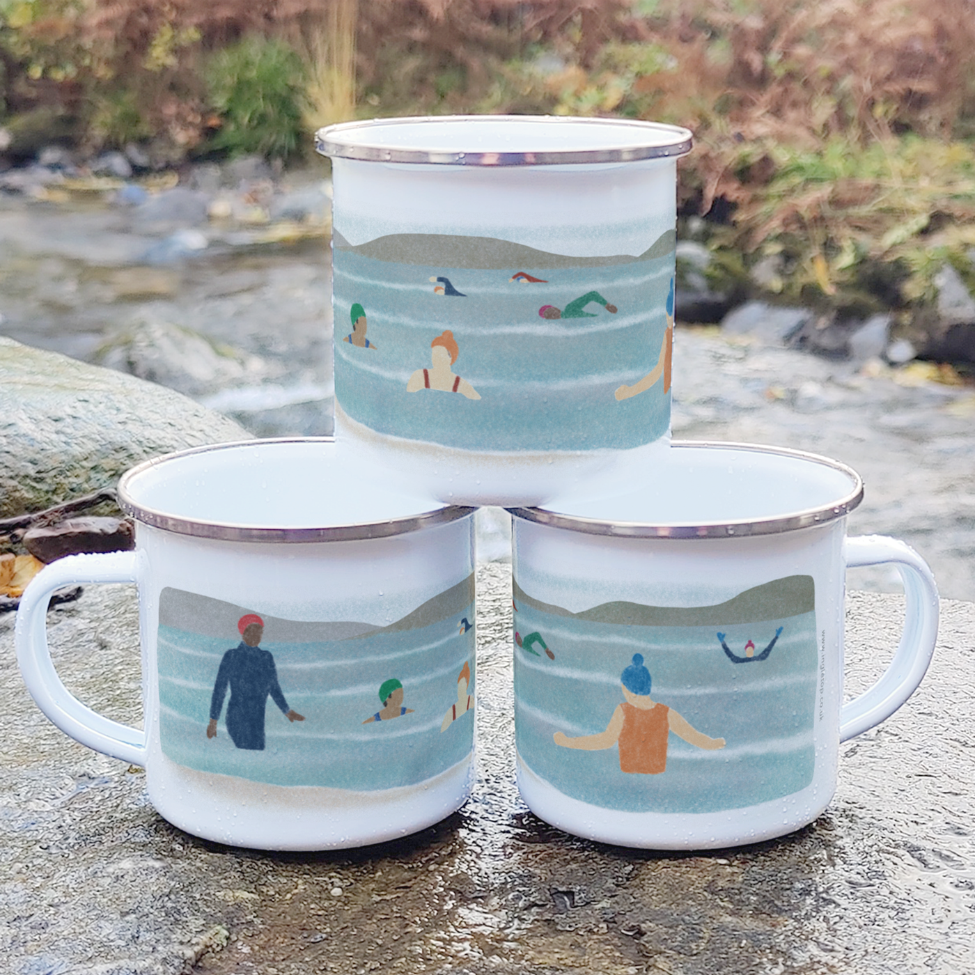 Three stacked enamel mugs, printed with an illustration of a group of eight wild swimmers, displayed outdoors on a rock