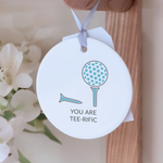 Circular ceramic decoration, with the message "You Are Tee-rific" and an illustration of two golf tees and a golf ball, hanging from a wooden peg