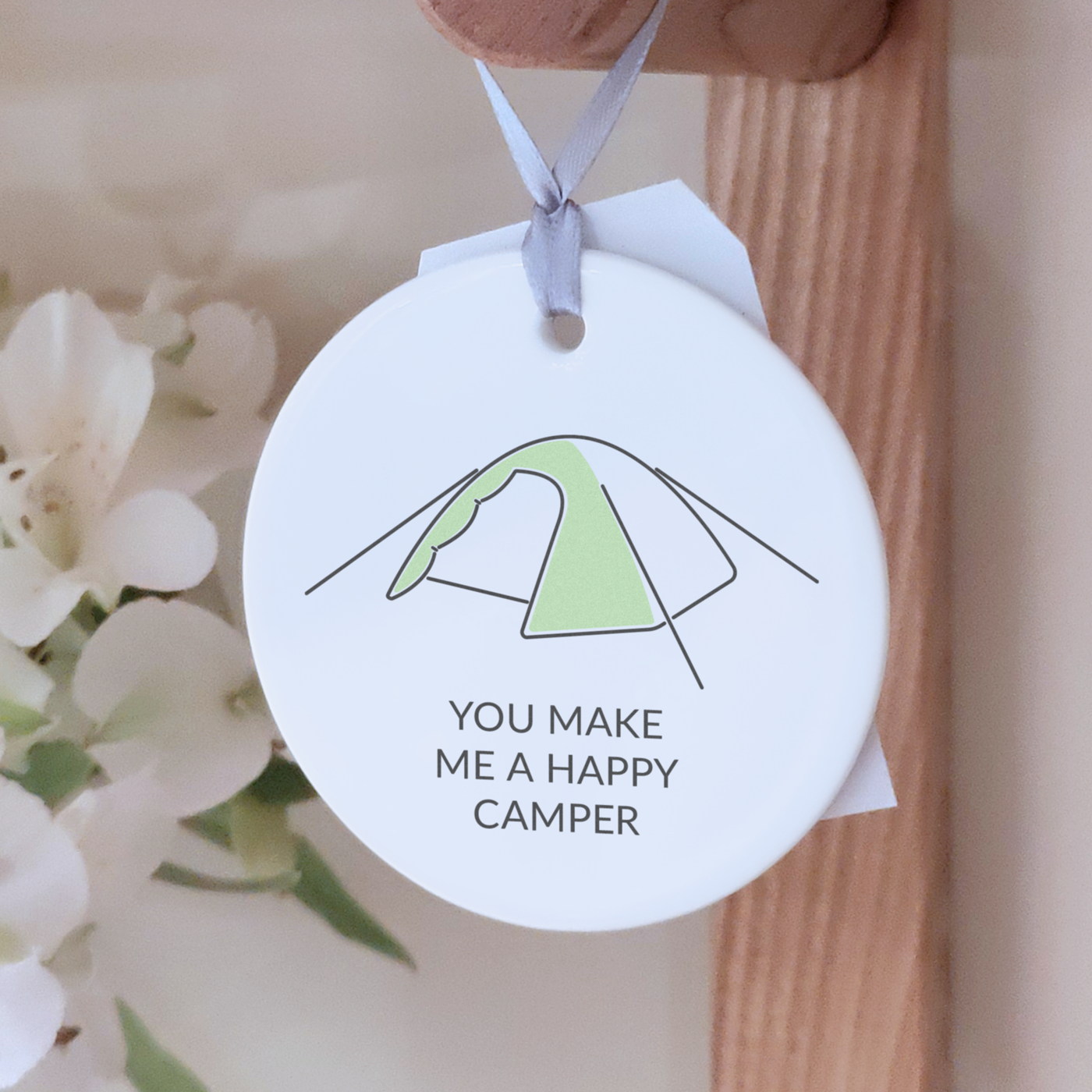 Round ceramic decoration with the message "you make me a happy camper" and an illustration of a tent, hanging on a wooden hook